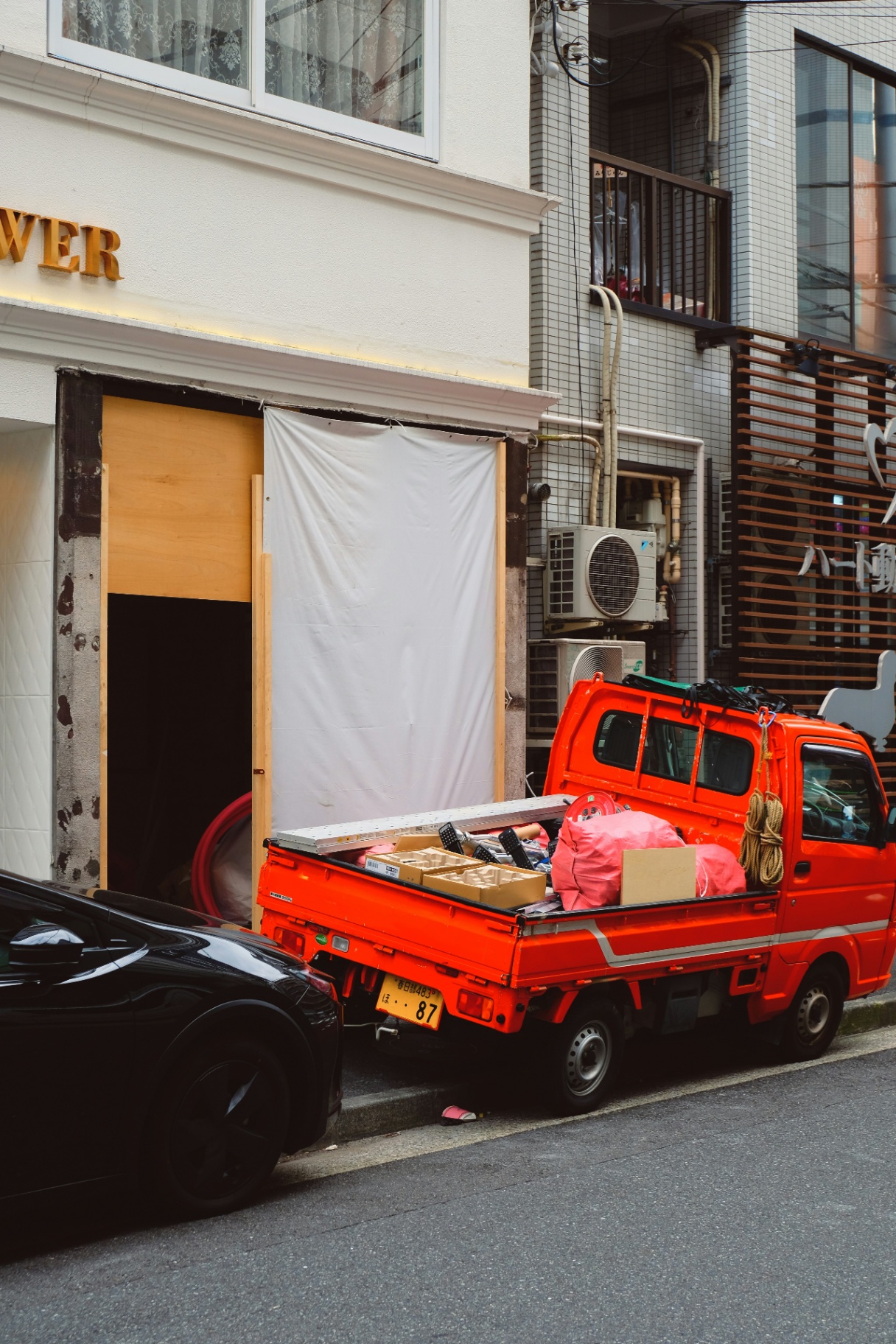 Orange Kei truck loaded with building materials in a narrow Tokyo alley