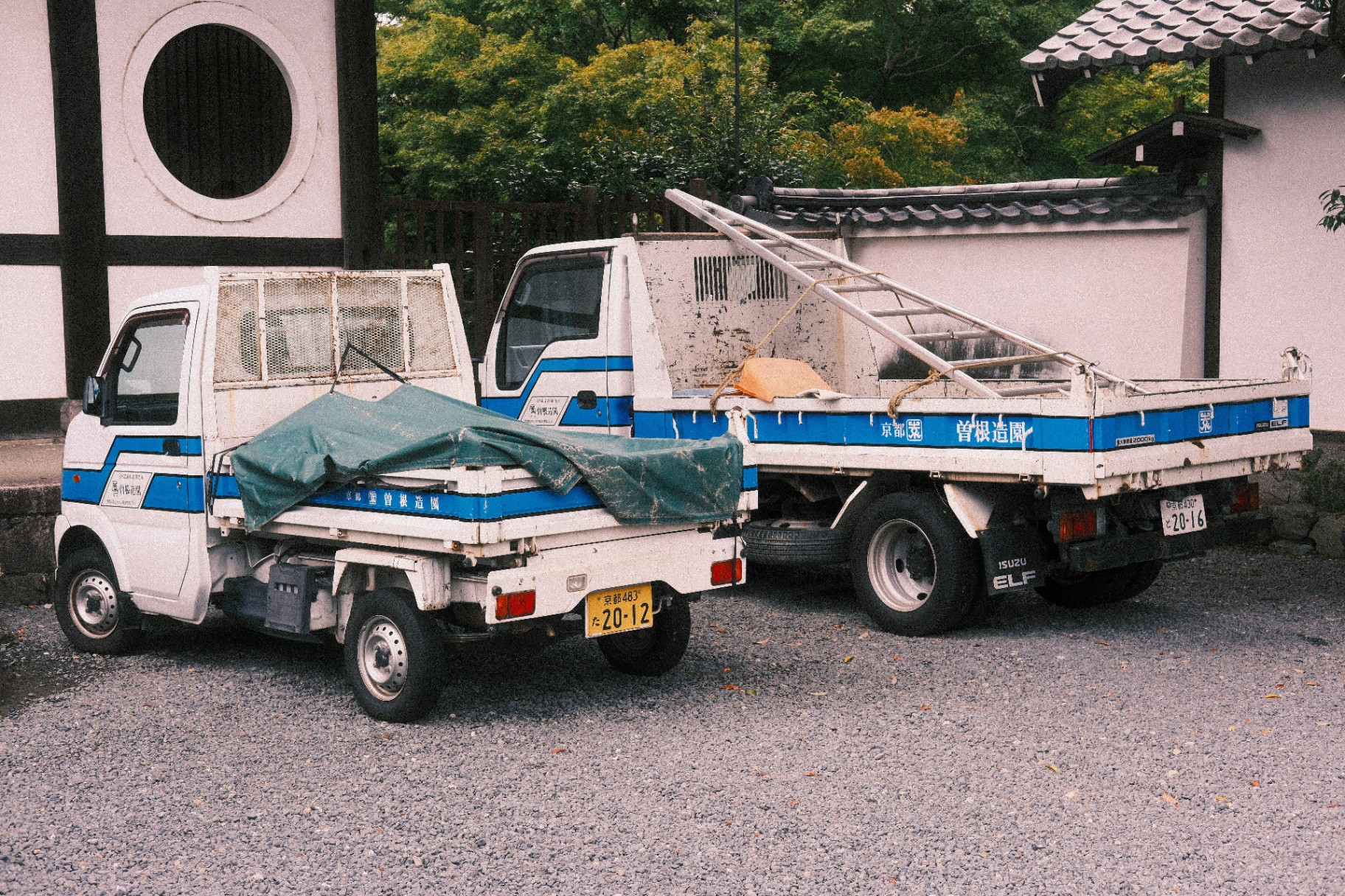 A pair of Japanese Kei work trucks parked at a Kyoto jobsite, proof of daily commercial use