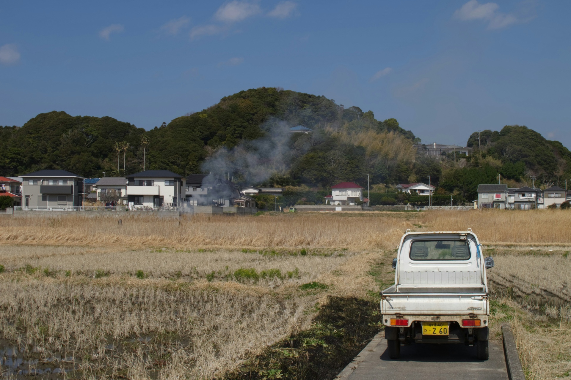 White 4WD Kei truck on a farm road beside rice fields in Japan