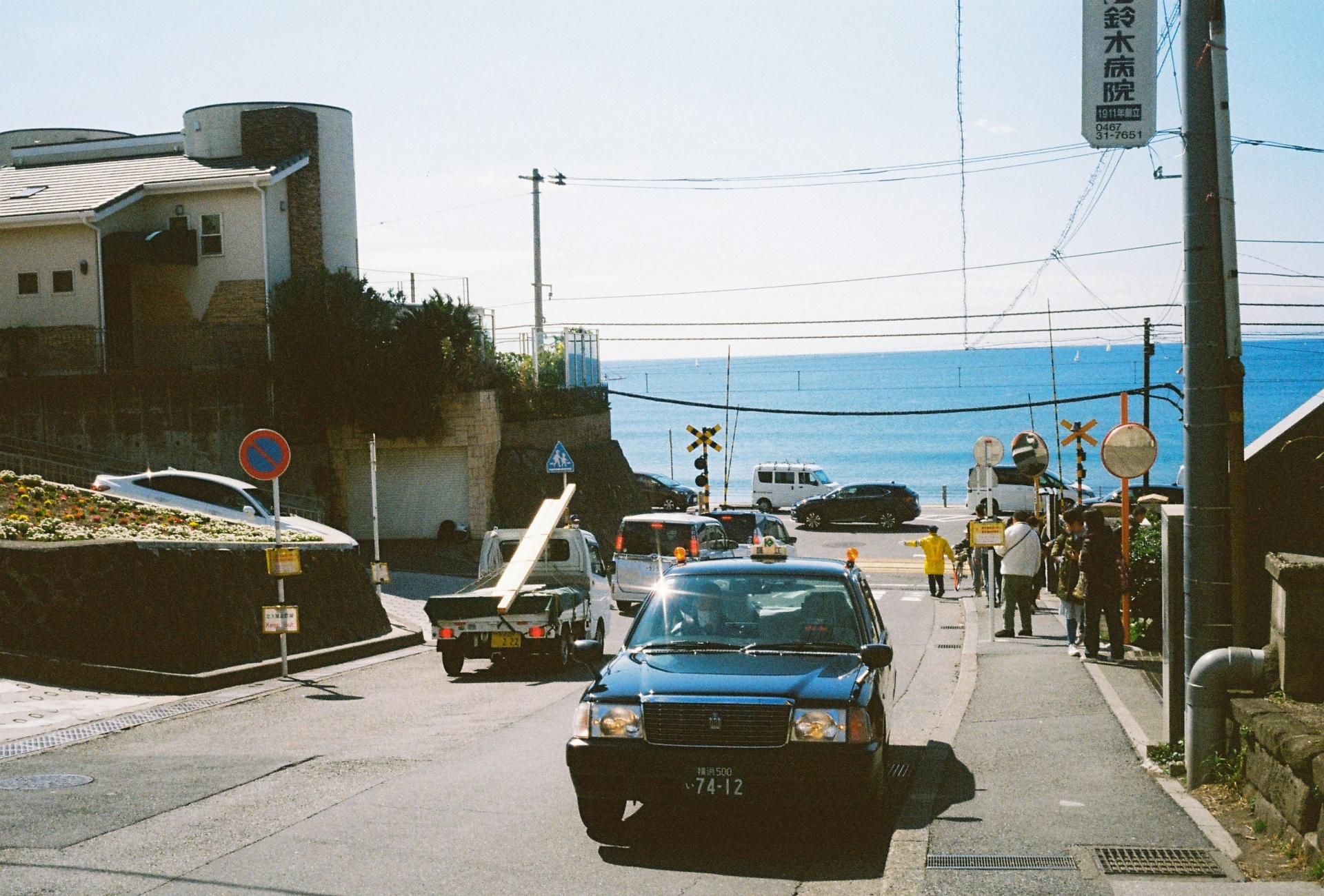 Kei truck and Kei vans parked on a narrow Japanese coastal street above the ocean