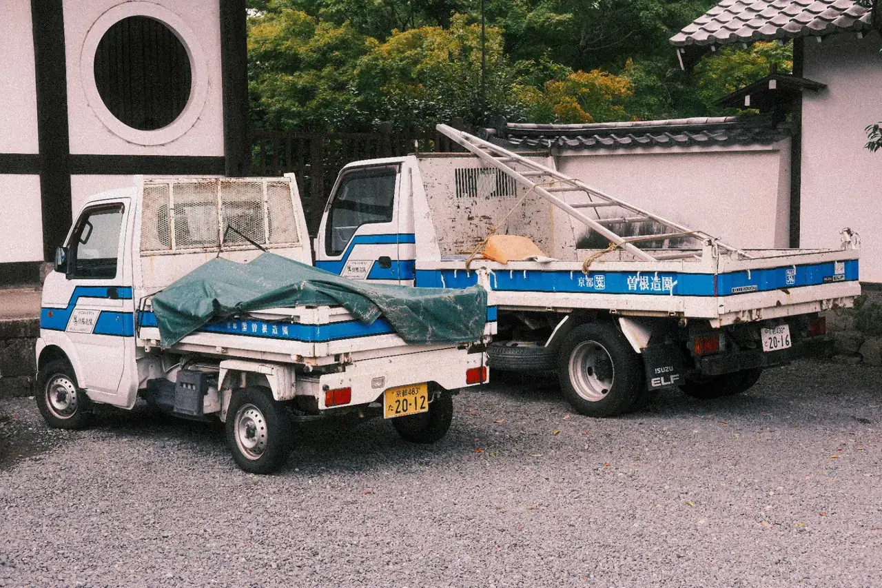 A pair of Japanese Kei work trucks parked at a Kyoto jobsite, proof of daily commercial use